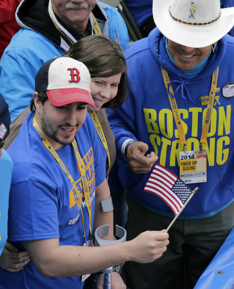 Boston Marathon bombing survivor Jeff Bauman waves an American flag alongside his fiancee Erin Hurley and Carlos Arredondo, right, the cowboy hat-wearing spectator who was hailed as a hero for helping the wounded after the bombings, near the finish line of the 118th Boston Marathon Monday, April 21, 2014 in Boston. (AP Photo/Charles Krupa)