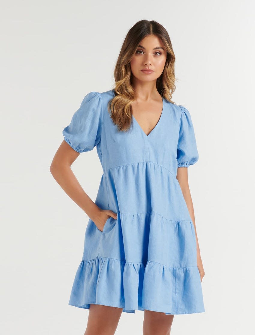 Woman stands in blue Tuscany Linen Mini Dress from Forever New, $129.99