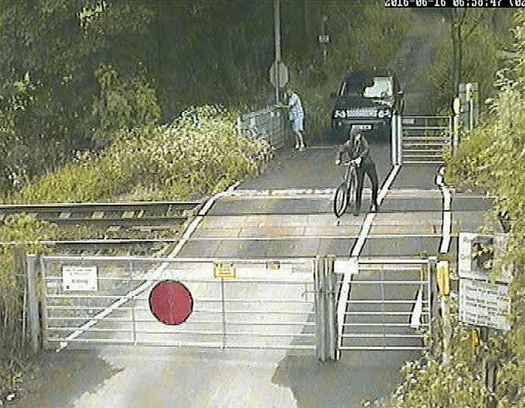 The cyclist is seen pushing his bike across the tracks after another man opens the gate for him (Network Rail/PA Wire) 