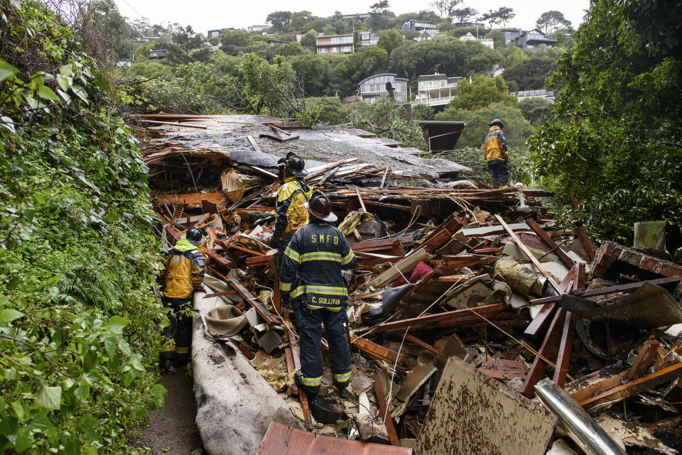 Southern Marin Fire Department members search a crushed house in the aftermath of a mudslide that destroyed three homes on a hillside in Sausalito, Calif., Thursday, Feb. 14, 2019. Waves of heavy rain pounded California on Thursday, filling normally dry creeks and rivers with muddy torrents, flooding roadways and forcing residents to flee their homes in communities scorched by wildfires. (AP Photo/Michael Short)