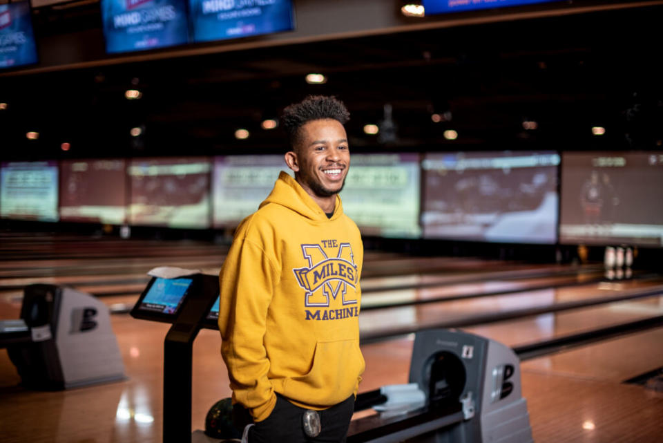 A man in a yellow sweatshirt smiling in front of a bowling alley