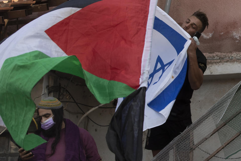 FILE - In this Friday, April 16, 2021 file photo, a man kisses the Israeli flag as protesters wave the Palestinian flag at the front gate of a Palestinian home occupied by Israeli Jews during a demonstration against the forcible evictions of Palestinians from their homes in the Sheikh Jarrah neighborhood of Jerusalem. A dispute over Israeli restrictions on Palestinian voters in east Jerusalem is threatening to cancel or delay the first Palestinian elections in more than 15 years. (AP Photo/Maya Alleruzzo, File)