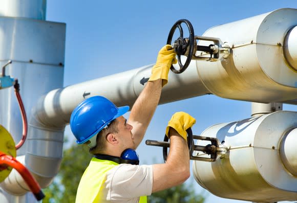 A man wearing a hard hat turning valves on a pipeline
