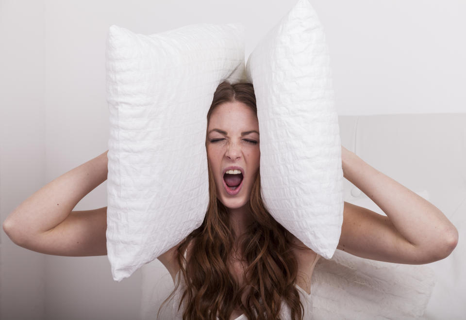 angry woman holds pillows to her ears due to extreme noise of the neighbours