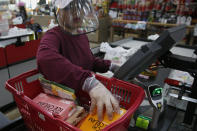 FILE - In this March 27, 2020, file photo, cashier Baby San wears a face shield and gloves as she scans items at grocery store Super Cao Nguyen, in Oklahoma City, due to concerns over the COVID-19 virus. Grocery workers across the globe are working the front lines during lockdowns meant to keep the coronavirus from spreading. (AP Photo/Sue Ogrocki, File)