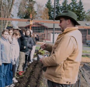  Neil Howe, or “Farmer Neil,” asks students a math question related to how many beans the students will plant. March 28, 2024. (Grace Deng/Washington State Standard)