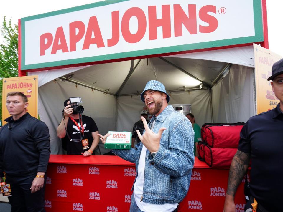 Travis Kelce poses in front of a Papa John's tent.