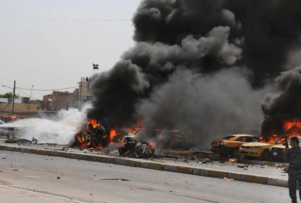 An Iraqi policeman looks at firefighters trying to extinguish burning vehicles moments after one in a series of bombs hit the Shiite stronghold of Sadr City, in Baghdad, Iraq, Tuesday, May 13, 2014. A wave of car bombings in mainly Shiite areas of Baghdad killed tens on Tuesday, officials said. (AP Photo/Karim Kadim)