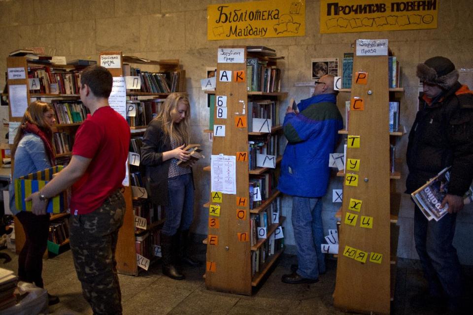 In this photo taken on Thursday, Feb. 6, 2014, Ukrainian protesters look at books organized on shelves in an improvised library set inside the Ukrainian House in Kiev. When the fervor flags for the protesters in Ukraine’s capital and they want to get away from the barricades for a little while, many of them are heading to an improvised library in one of the buildings seized by demonstrators. (AP Photo/Emilio Morenatti)