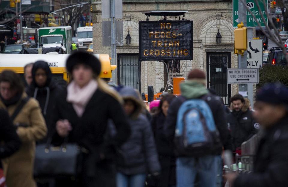 With a recently placed warning sign in the background, pedestrians in foreground walk off the street to a subway station at the busy intersection of W. 96th Street and Broadway in the Upper West Side of New York Monday, Jan. 27, 2014. New York Mayor Bill de Blasio, in the wake of 11 pedestrian deaths in the city already in 2014, is taking direct aim at not just drivers but pedestrians, with a crackdown that has resulted in the first jaywalking tickets some residents have ever seen. (AP Photo/Craig Ruttle)