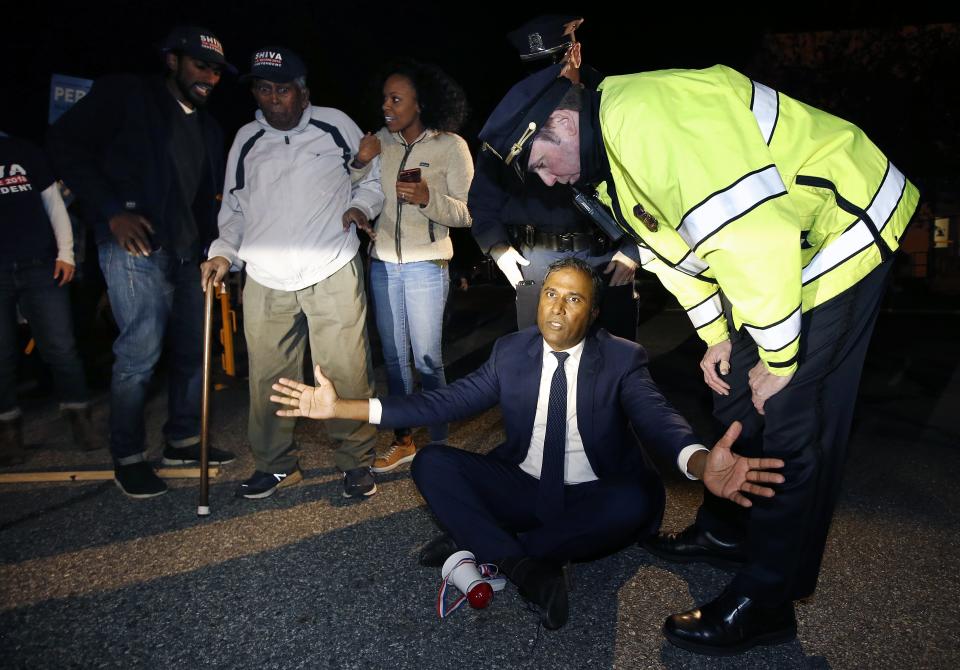 Independent candidate for the U.S. Senate from Massachusetts Shiva Ayyadurai sits in the road to block the car of incumbent Sen. Elizabeth Warren before a debate between Warren and her Republican opponent Geoff Diehl in Boston, Friday, Oct. 19, 2018. (AP Photo/Michael Dwyer)