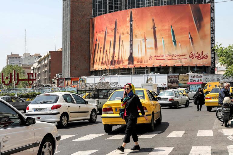 Una mujer cruza un paso de peatones cerca de un cartel que muestra misiles balísticos iraníes en servicio con nombres, con un texto en árabe que dice 