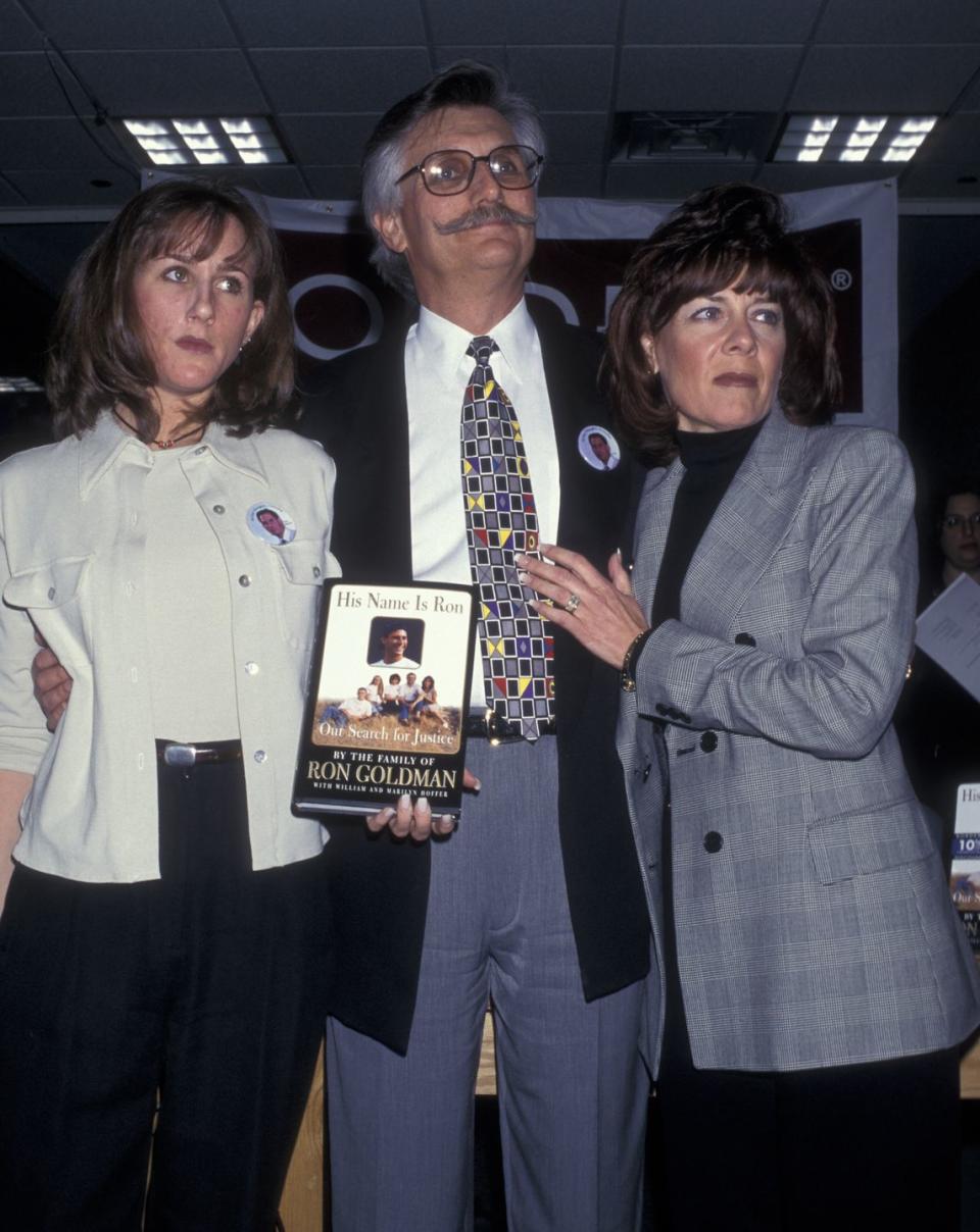 kim goldman, fred goldman, and patti goldman stand together, fred holds a book in front of him as all three people look to the right