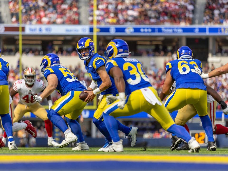 Matthew Stafford prepares to hand the ball to a running back while the offensive line blocks during a game.