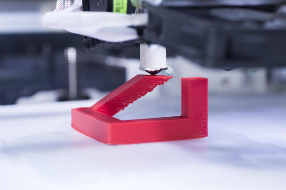 Close-up of a 3D printer printing an unidentifiable red plastic object.