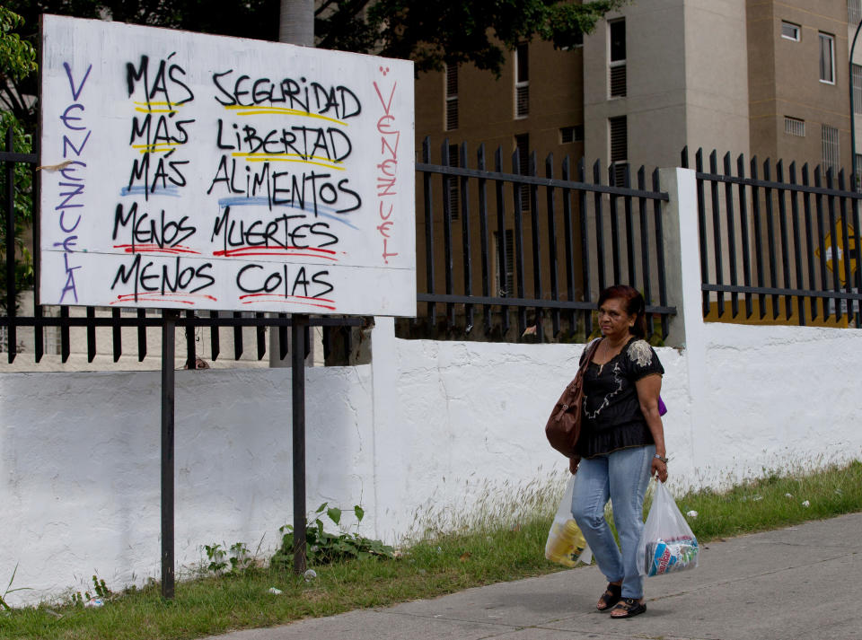 A woman carries powdered milk and cooking oil she bought from the state-run supermarket Bicentenario as she walk by a poster that reads in Spanish "Venezuela, more security, more freedom, more food, fewer deaths, less lines" near the Petare shantytown in Caracas, Venezuela, Friday, Jan. 16, 2015. Venezuela’s crisis has been long in the making. Even before collapsing oil prices strangled its foreign revenue stream, the country was stuck in a year-old recession and its inflation rate racing toward triple digits. (AP Photo/Fernando Llano)