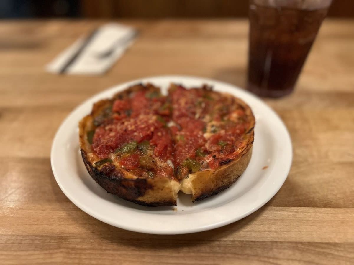 Personal-sized Chicago-Style Pizza on a white porcelain plate, Lou Malnati’s, Lincolnwood, Illinois, selective focus, on a wooden table with a glass of soda on the right and utensils on the top left, blurred