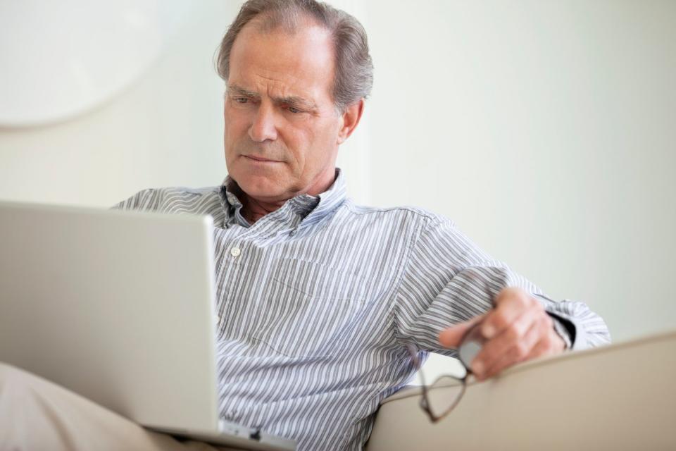 A person seated on a couch who's critically reading content from a laptop on their lap.