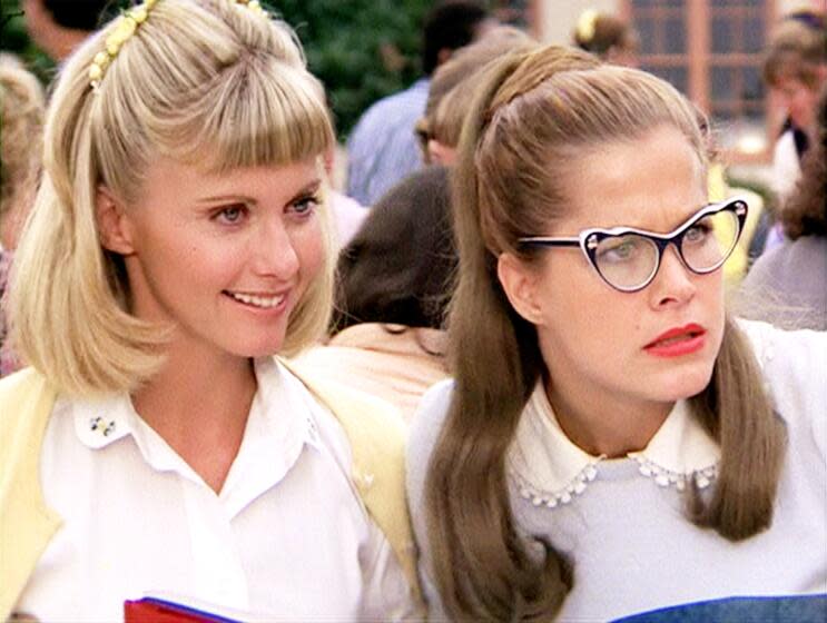 Photo still of two women, one with short blond hair with bangs another with long brown hair and glasses, from "Grease"