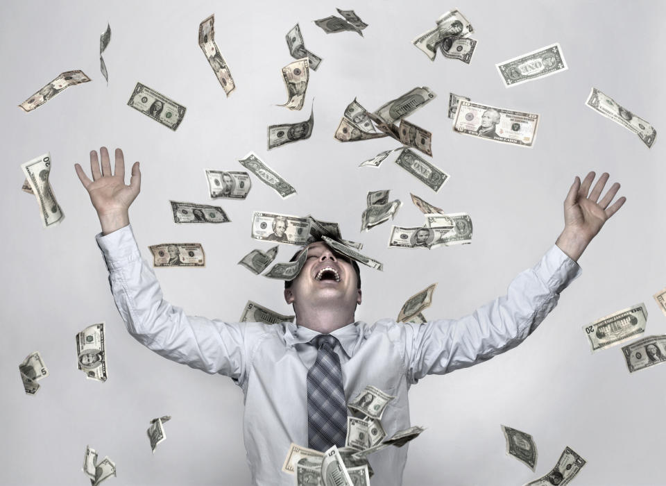 A man wearing a shirt and tie throws American dollar bills in the air. He is laughing.