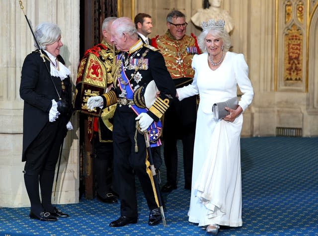 The King smiles as he chats happily to Black Rod, while Camilla links her arm with her husband's