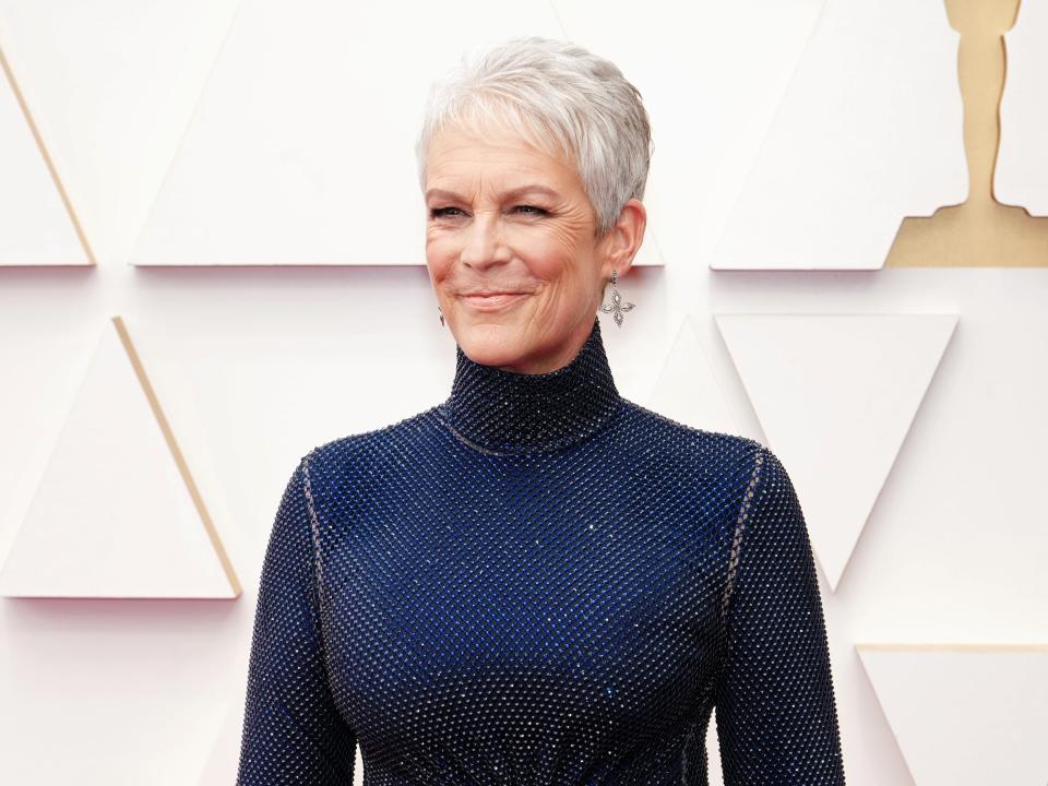 Jamie Lee Curtis in high-neck sparkly blue down in front of white Oscars background