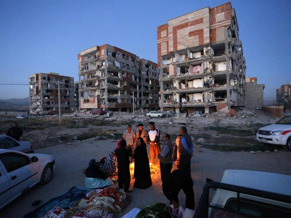 Survivors of the earthquake warm themselves in front of destroyed buildings at the city of Sarpol-e-Zahab in western Iran (AP)