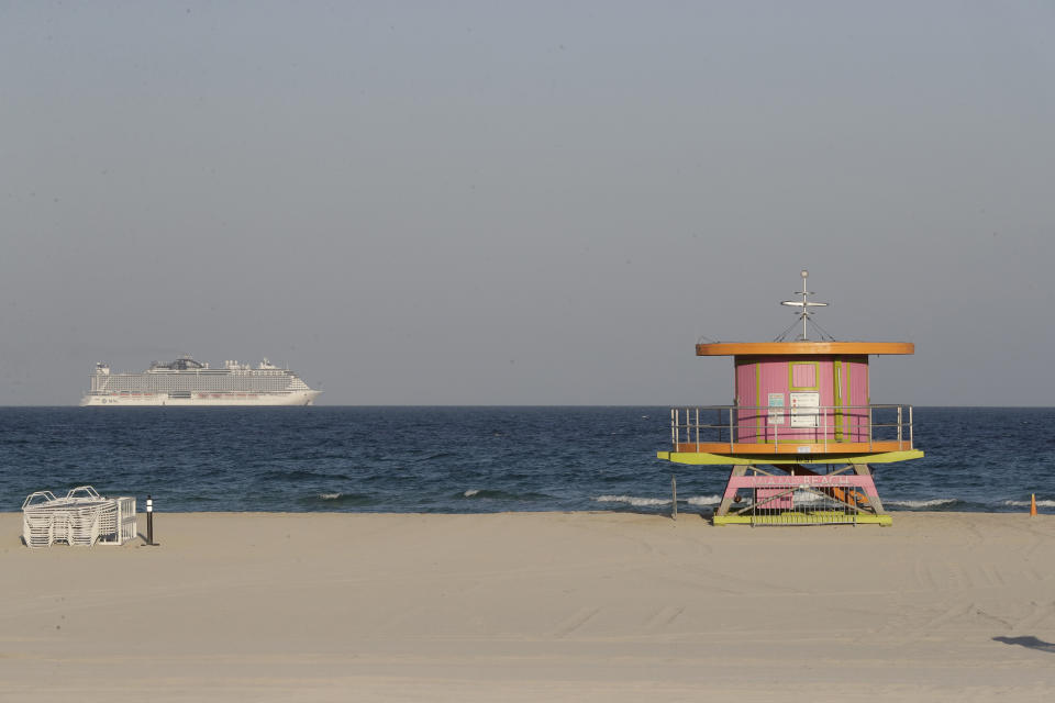 A cruise ship is shown out at sea, beyond a lifeguard tower along a closed beach Wednesday, March 25, 2020, in Miami Beach, Fl. (AP Photo/Wilfredo Lee)