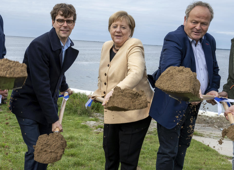 German Chancellor Angela Merkel, center, Georg Guenther, Chairman of the Junge Union Mecklenburg-Vorpommerns and the Mayor of the municipality of Ummanz, Holger Kliewe, right, perform the symbolic ground-breaking ceremony for the extension of the cycle path in the municipality near Waase on the island of Ummanz, Germany, Tuesday, Sept. 21, 2021. (Stefan Sauer/dpa via AP)