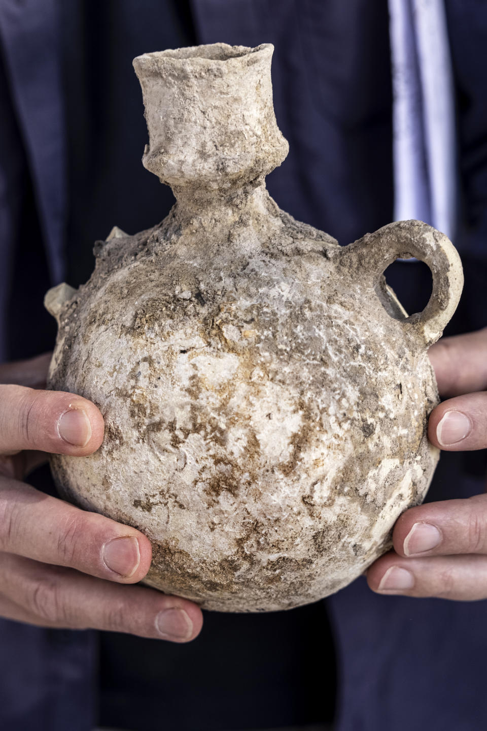 An Israel Antiquities Authority employe holds a jar from a massive ancient winemaking complex dating back some 1,500 years in Yavne, central, Israel, Monday, Oct. 11, 2021. Israeli archaeologists said the complex includes five wine presses, warehouses, kilns for producing clay storage vessels and tens of thousands of fragments and jars. (AP Photo/Tsafrir Abayov)