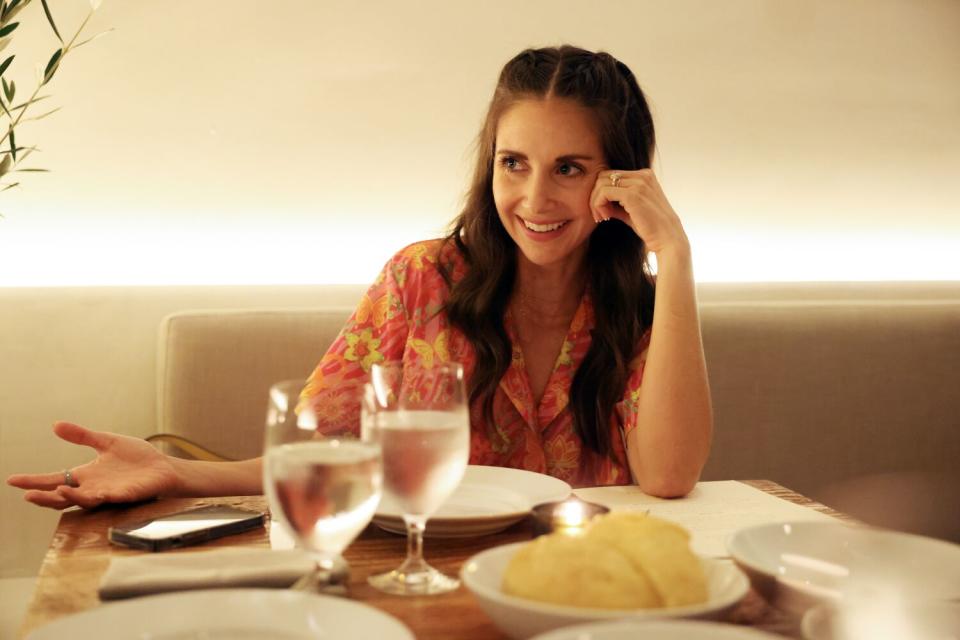 Alison Brie sitting in a booth and talking to someone off-camera.