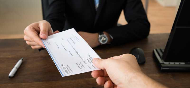 A hand holds out a check to a man in a business suit.