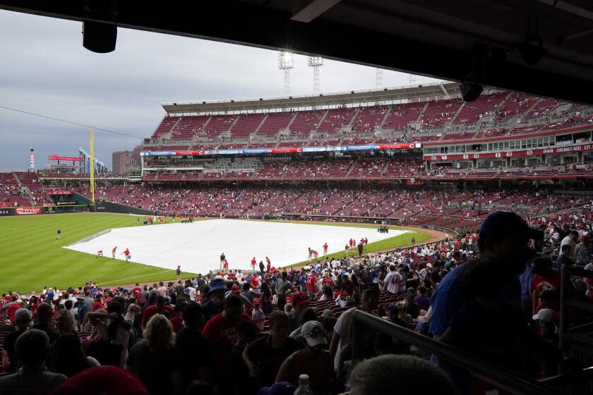 The grounds crew pull the tarp over the field ahead of a rain delay during a game between the Dodgers and Reds