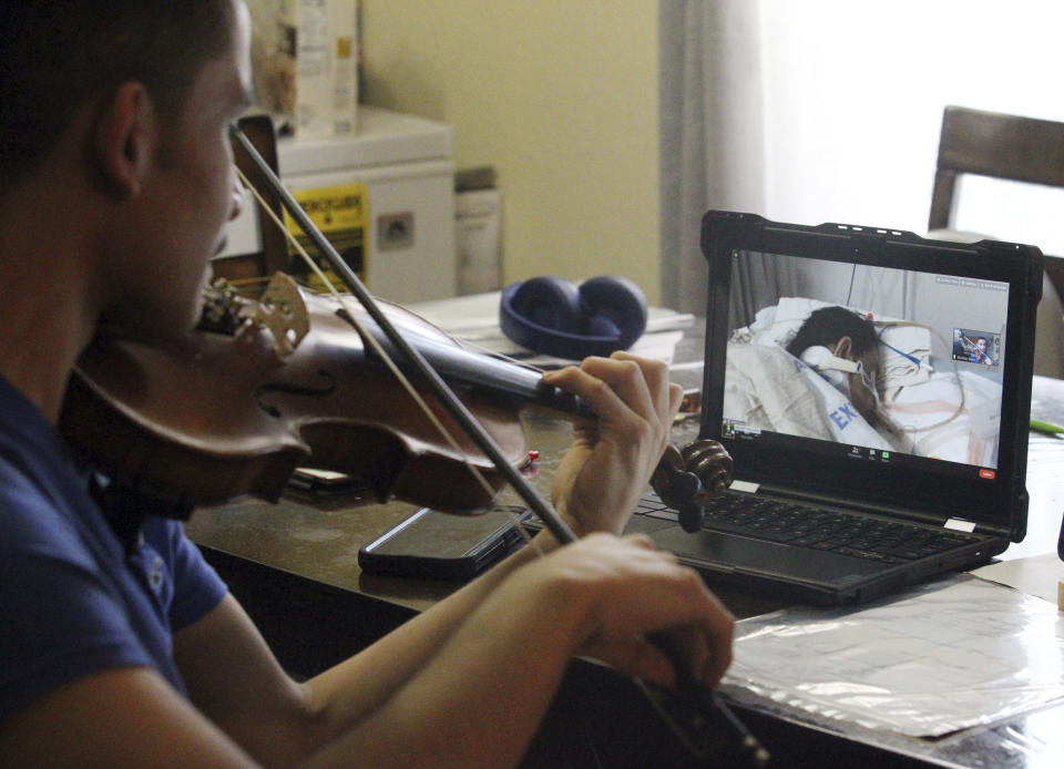 Emilian Sosa, 14, plays the violin for his mother seen through a zoom monitor screen at her hospital bed on Wednesday, Jan. 27, 2021, in McAllen, Texas. Sosa says his mother Erika Calderon has been battling COVID-19 for more than 20 days and needs Extracorporeal Membrane Oxygenation (ECMO) therapy to help her recover. (Delcia Lopez/The Monitor via AP)