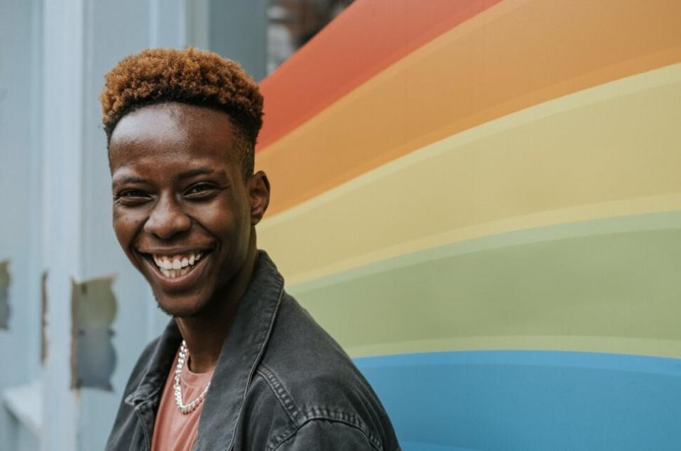 LGBTQIA+ community members deserve safe travel experiences too! Check out these countries in Africa that are the most accepting and safest. Pictured: a Black man smiling with a rainbow mural behind him.