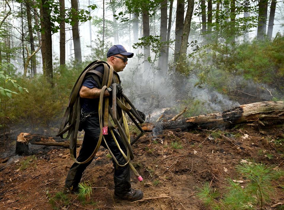Marlborough firefighter Rob Fadgen carries a line of hose by a burning log as a brush fire burns in the Marlborough-Sudbury State Forest for a second day, Aug. 20, 2022. Firefighters ran lines of hose deep into the forest to battle the blaze.