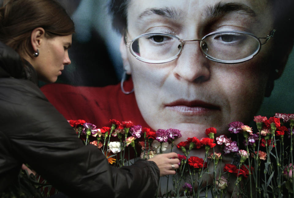 FILE- In this Oct. 7, 2009, file photo, a woman places flowers before a portrait of slain Russian journalist Anna Politkovskaya, in Moscow. Politkovskaya, who won international acclaim for her reporting on the human rights abuses in the Russian republic of Chechnya was shot dead in the elevator of her Moscow apartment building. (AP Photo/Pavel Golovkin, File)