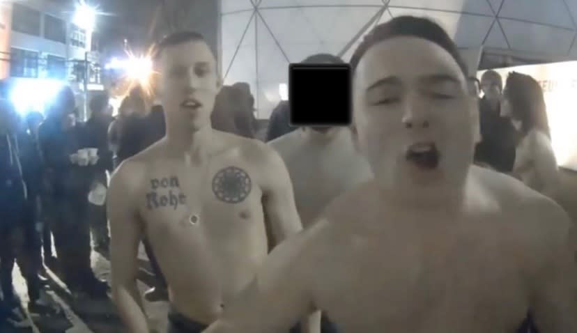 McCaffrey, shirtless, yells into a camera at an art exhibit at the Museum of the Moving Image in Queens, New York, in February 2017. Next to him is a man with a chest tattoo of a sonnenrad. (Photo: Screenshot)