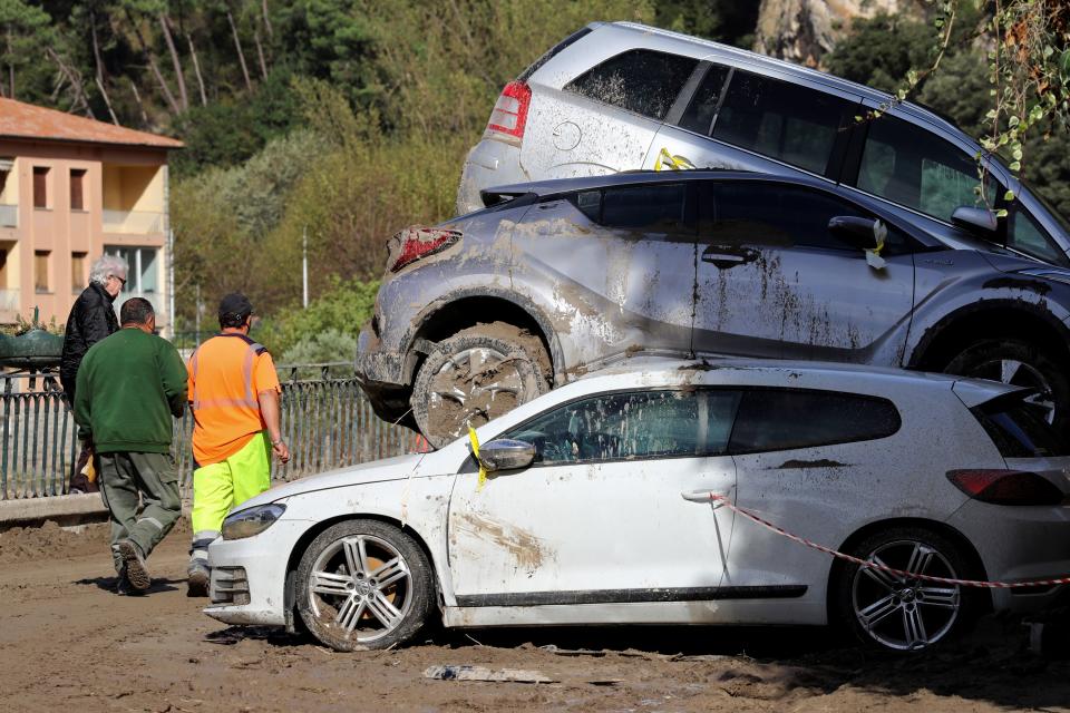 Residents walk past piled -p cars that were washed on top of each other in the floods.