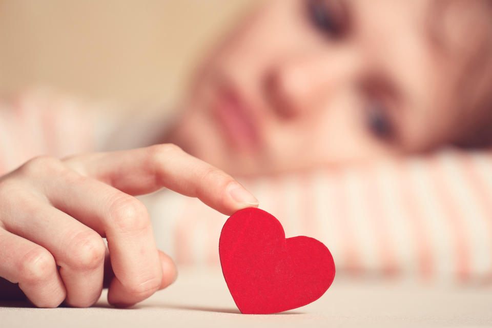 Sad girl is holding heart symbol by her finger and looking at it. Love and relationships concept