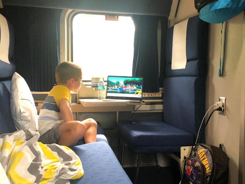 kid sitting on blue couch in a room on a train watching a show on a laptop