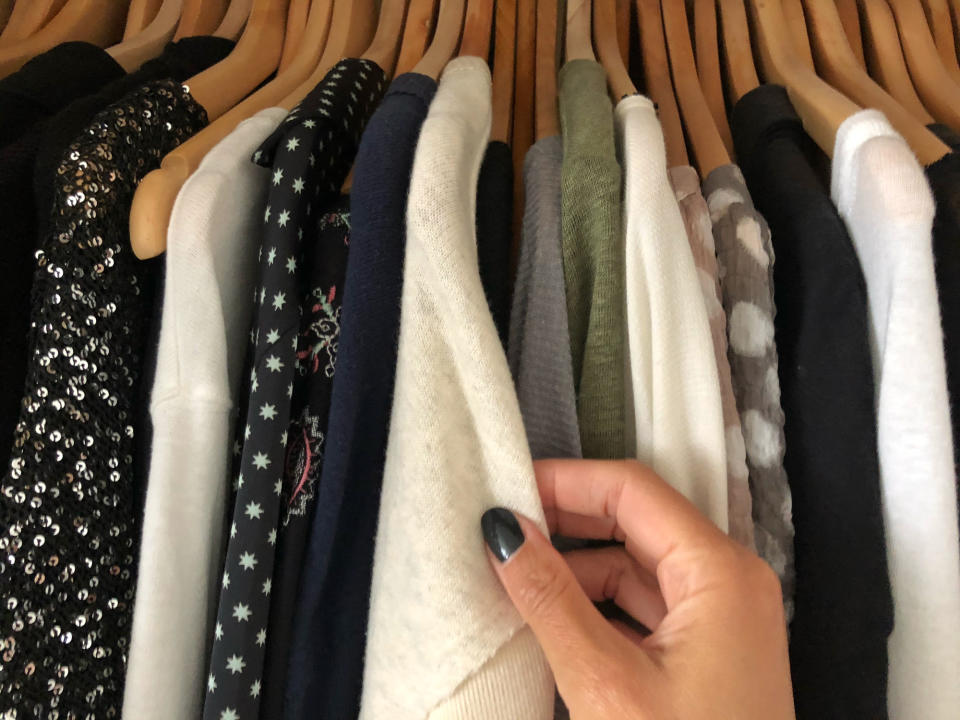 Person's hand browsing through a variety of clothes on hangers