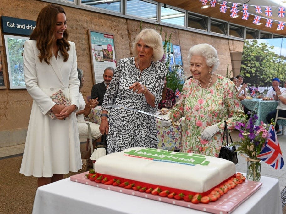 Queen Elizabeth cuts a cake with a sword as Kate Middleton and Camilla look on