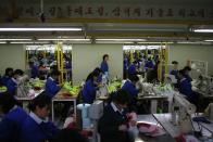 North Korean employees work in a factory of a South Korean company at the Joint Industrial Park in Kaesong industrial zone, a few miles inside North Korea from the heavily fortified border December 19, 2013. Kaesong, with investors from South Korea, was a rare source of hard currency for North Korea. It was established even though North Korea is technically still at war with South Korea, one of the world's richest countries, since the 1950-53 Korean War ended not in a treaty but a truce. Since it opened in 2004, the Kaesong complex has generated about $90 million annually in wages paid directly to the North's state agency that manages the zone. The banner reads, "The first priority is high quality, the second priority is also high quality". REUTERS/Kim Hong-Ji (NORTH KOREA - Tags: POLITICS BUSINESS EMPLOYMENT)