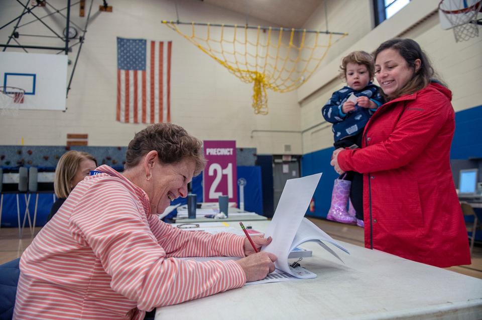 Hillary Jacobson, left, a Precinct 21 election worker, checks in voter Rachel Welt as Welt holds her daughter Sophie, 2, at Brophy Elementary School in Framingham, March 5, 2024.