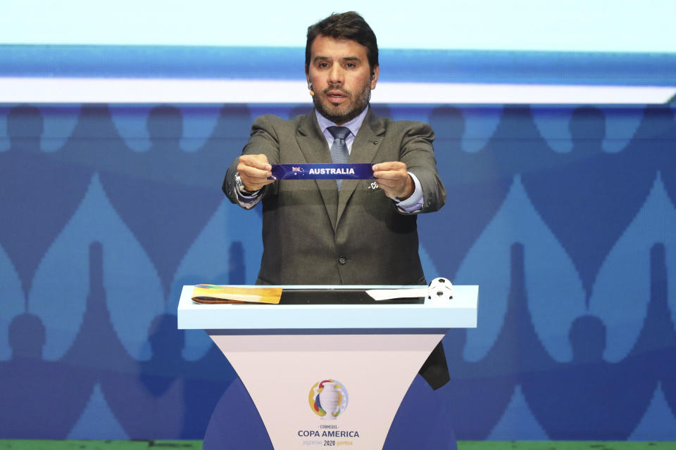 Conmebol Competitions' director Hugo Figueredo holds up the team name of Australia during the draw for the 2020 Copa America soccer tournament in Cartagena, Colombia, Tuesday, Dec. 3, 2019. Australia will participate in the continental championship to be held in Colombia and Argentina from June 12 to July 12 next year. (AP Photo/Fernando Vergara)