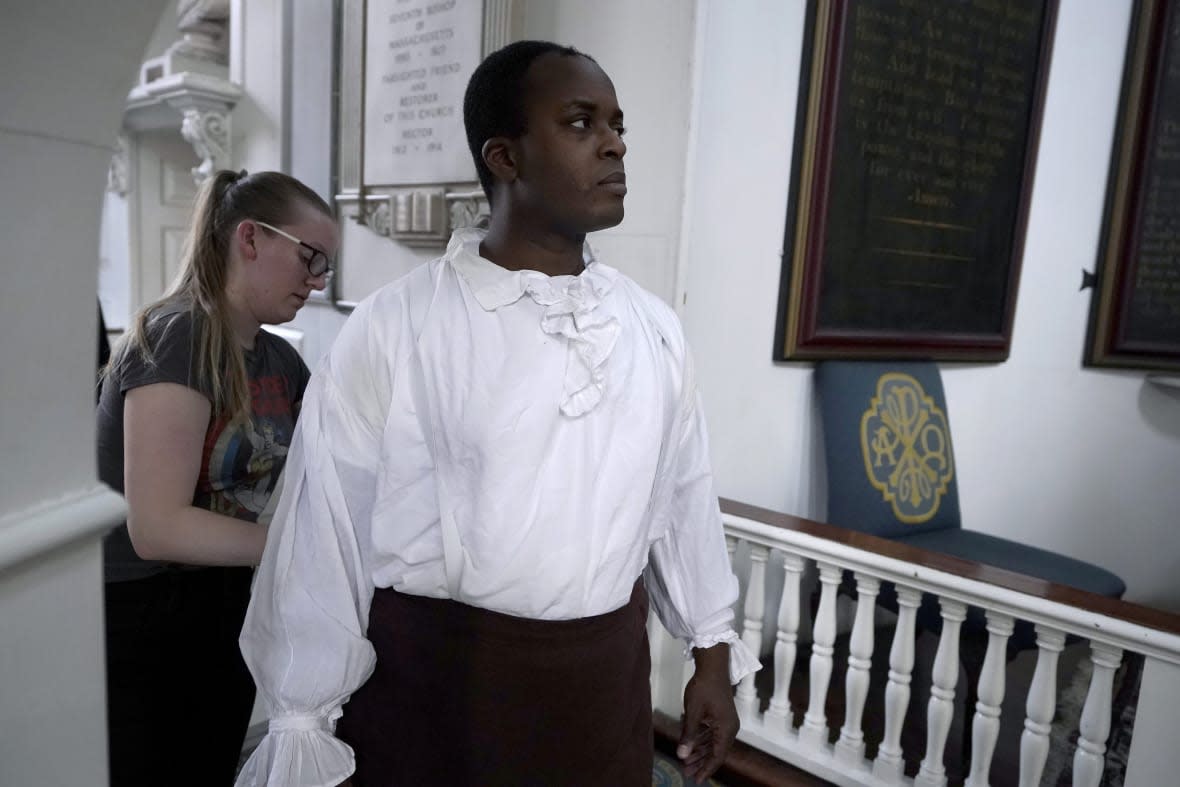 Actor Nathan Johnson, in the role of Cato, front, receives assistance with his costume from costume designer Christina Beam, behind left, before the start of a dress rehearsal of the play “Revolution’s Edge” Monday, June 12, 2023, at Old North Church, in Boston’s historic North End neighborhood. (AP Photo/Steven Senne)