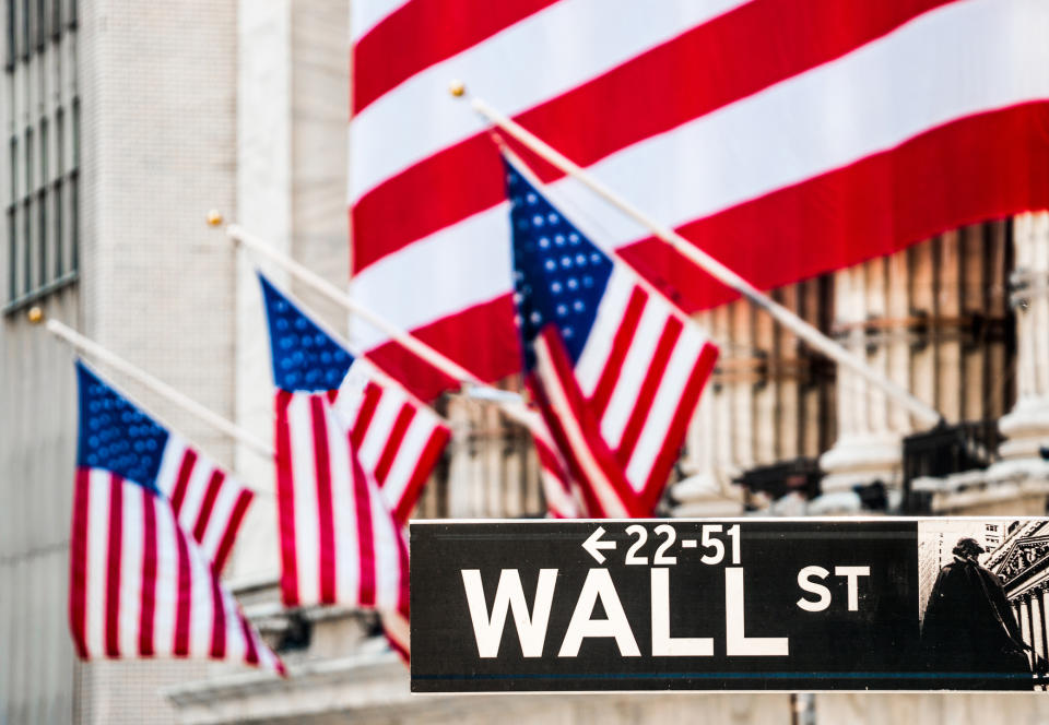 The facade of the New York Stock Exchange draped a large American flag, with the Wall St. street sign in the foreground.