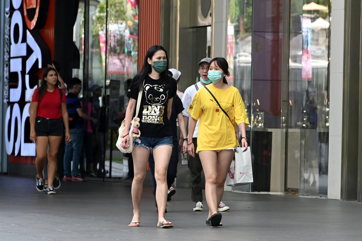 People wearing surgical masks amid fears about the spread of the COVID-19 coronavirus walk past a shopping mall in Singapore on 26 February. (Photo: AFP)