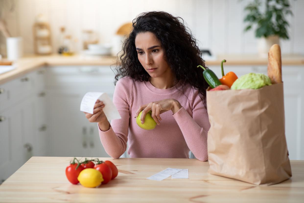 save money Concerned Young Woman Checking Bills In Kitchen After Grocery Shopping, Millennial Female Sitting At Table In Kitchen, Frustrated About Expensive Vegetables And Fruits, Closeup Shot, Selective Focus